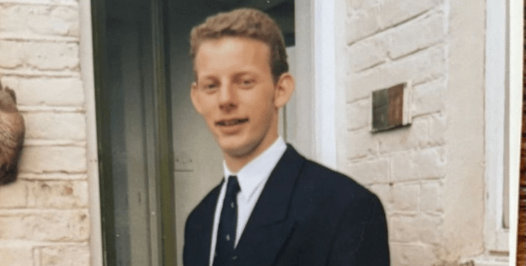 A teenage Captain Simon stands outside his house in school uniform, smiling at the camera
